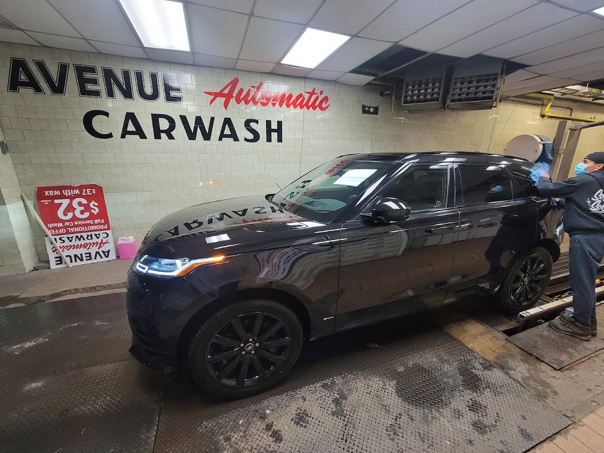 A Range Rover being hand-dried by an Avenue Car Wash team member inside the facility, with the Avenue Automatic Carwash wall signage visible